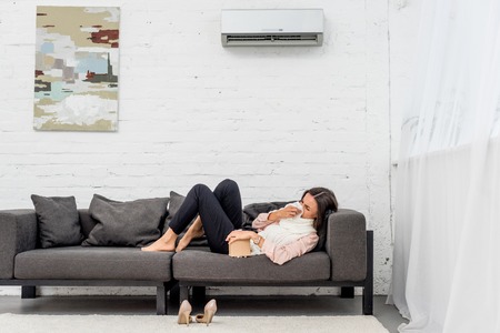 Side view of sick young woman lying on couch at home