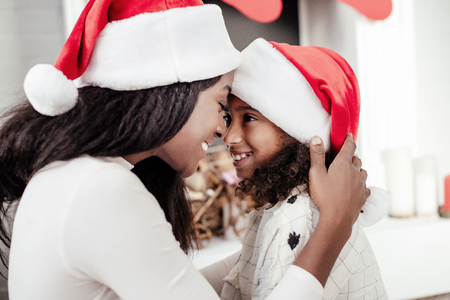 Side view of smiling African American mother and daughter in Santa Claus hats looking at each other at homeの写真素材
