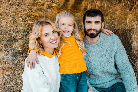 Portrait of happy farmer family sitting on hay stacks at ranch