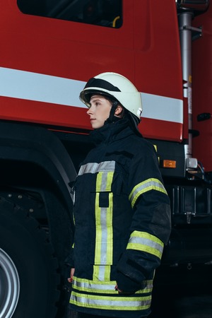 Side view of female firefighter in helmet standing at fire stationの写真素材