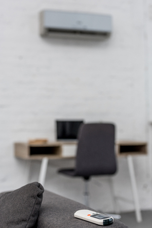 Close-up shot of air conditioner remote control lying on couch with workplace on backgroundの写真素材