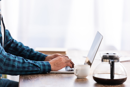 Close-up partial view of man in checkered shirt using laptop at homeの写真素材