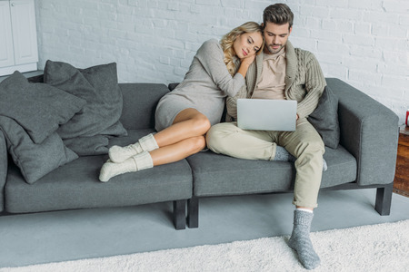 Affectionate couple watching something on laptop on sofa in living roomの写真素材