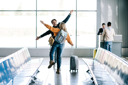 Happy young friends with backpacks greeting each other in airportの写真素材