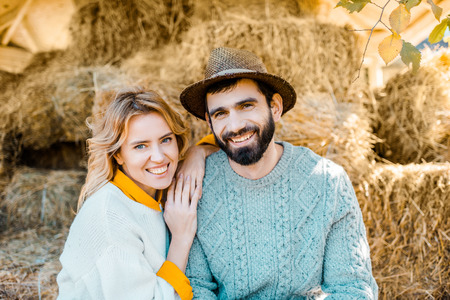 Portrait of happy couple of farmers looking at camera while sitting on stacks of hay at farmの写真素材