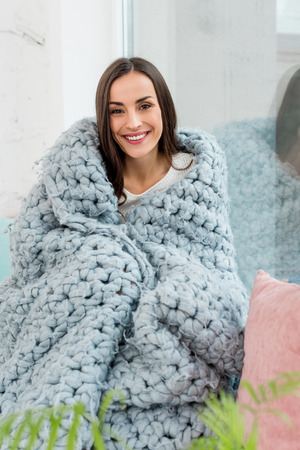 Happy young woman sitting on windowsill covered in blanket