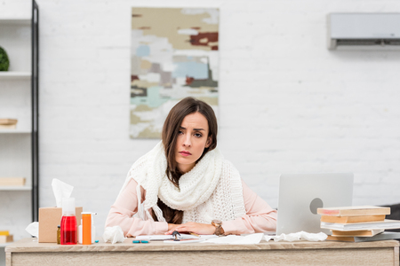 Sick young businesswoman looking at camera while sitting at workplaceの写真素材