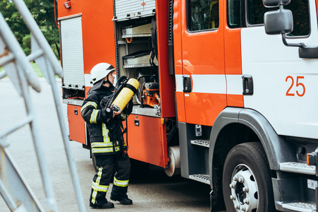 Female firefighter in protective uniform putting fire extinguisher into truck on street