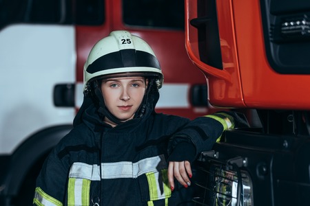 Portrait of female firefighter in helmet leaning on truck at fire stationの写真素材