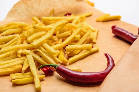 Tasty french fries with spicy peppers on parchment paper on white backgroundの写真素材