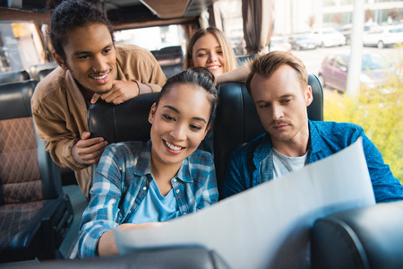 Smiling multiculutral friends looking at map during trip on travel bus