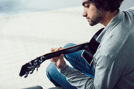 handsome man playing acoustic guitar at homeの写真素材