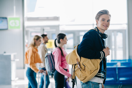 Handsome young man with backpack smiling at camera while traveling with friends