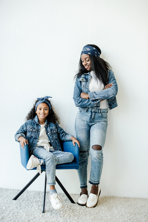 Smiling African American mother standing near daughter on chair at homeの写真素材