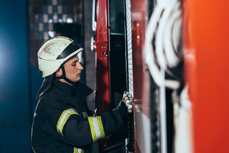 Side view of fireman in uniform closing truck at fire department