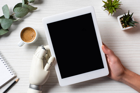 Partial view of businessman with prosthesis arm using digital tablet with blank screen at table with...