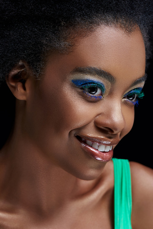 Portrait of smiling African American model with bright blue eyes shadows isolated on black backgroundの写真素材