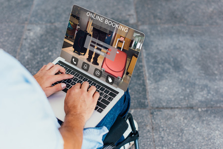 Cropped image of man in wheelchair using laptop with online booking website on streetの写真素材