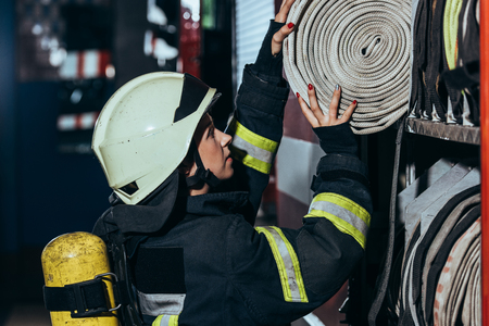 Side view of female firefighter putting water hose into truck at fire stationの写真素材