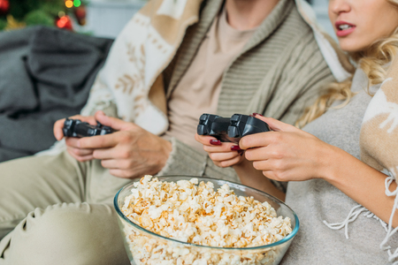 Cropped shot of couple with popcorn playing video games together on couch at homeの写真素材