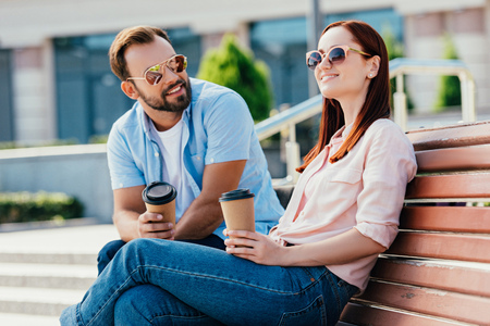 Smiling handsome boyfriend in wheelchair and girlfriend with disposable coffee cups on streetの写真素材