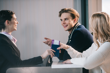 Smiling young couple looking at worker at check-in desk in airportの写真素材