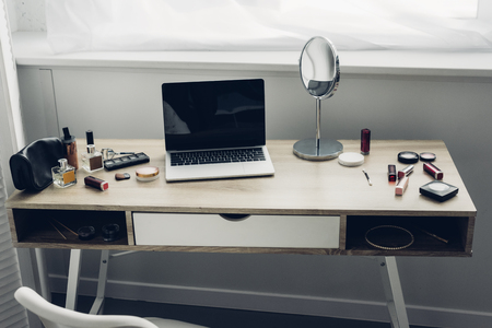 Close-up shot of modern workplace with laptop and makeup supplies at homeの写真素材