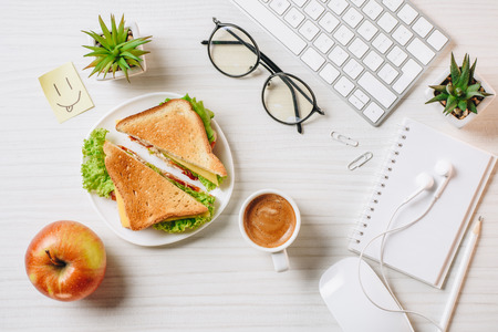 Top view of workplace with sandwich, paper coffee cup, apple and symbol of smile at table in officeの写真素材