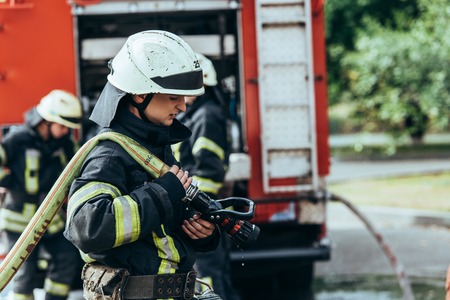 Selective focus of male firefighter in helmet with water hose on street
