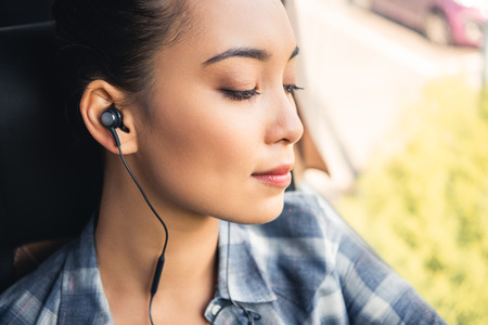Selective focus of Asian female traveler listening music in earphones during trip on busの写真素材