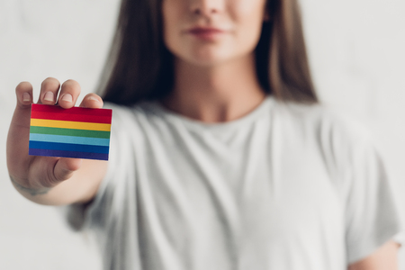 Close-up shot of young transgender man holding card with pride flag on white background