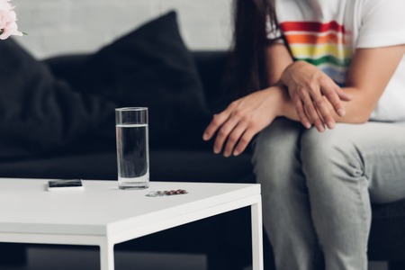 Cropped shot of man in t-shirt with pride flag sitting in front of glass of water and pillの写真素材