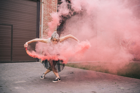 Attractive young female dancer dancing in pink smoke on streetの写真素材