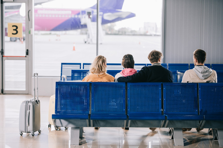 Back view of young people sitting and waiting for flight in airport terminalの写真素材
