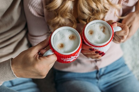 Cropped image of couple clinking with cups of cappuccino at home, Christmas conceptの写真素材