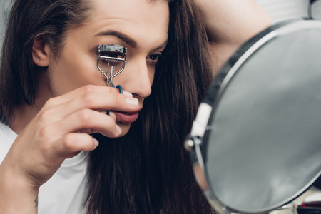 Young transgender man at home applying makeup