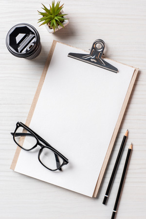 Top view of paper coffee cup, pencils, potted plant and empty clipboard at table in officeの写真素材