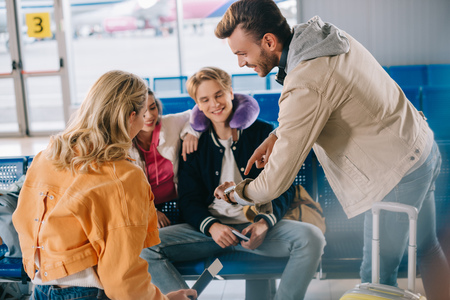 Smiling young people checking wristwatch while waiting for flight in airportの写真素材