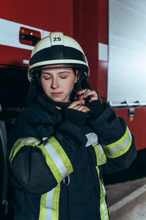 Portrait of female firefighter in uniform checking helmet at fire departmentの写真素材