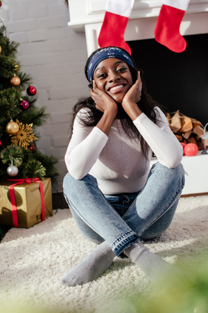 Smiling attractive African American woman resting chin on hands and looking at camera at home, Christmas conceptの写真素材