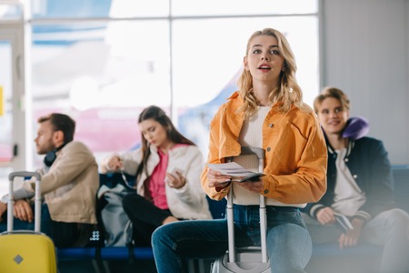Girl with passport and boarding pass sitting on suitcase in airportの写真素材