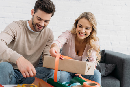 Smiling couple preparing Christmas gift box together at homeの写真素材
