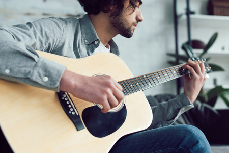 Handsome guitarist playing acoustic guitar at homeの写真素材