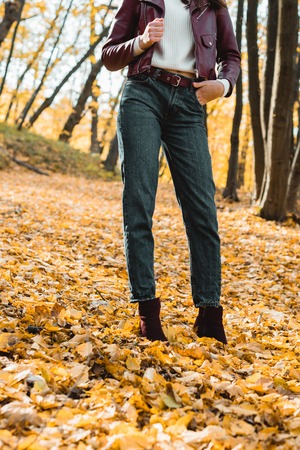 Cropped image of fashionable woman in jeans and leather jacket posing in autumnal parkの写真素材