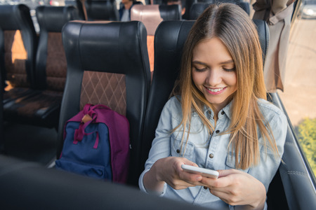 Happy young woman using smartphone while sitting on travel busの写真素材