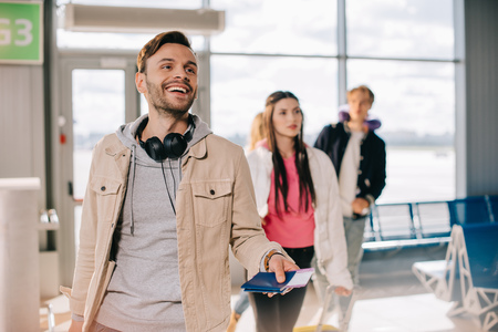Smiling young man holding passports and boarding passes in airport terminalの写真素材