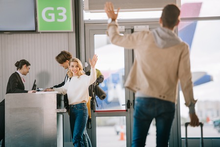 Happy young friends waving hands at check-in desk in airportの写真素材