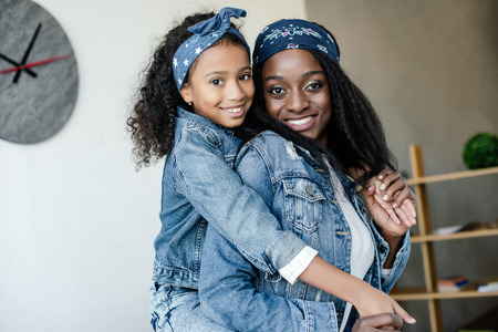 Cute African American kid hugging smiling mother in similar clothing at homeの写真素材