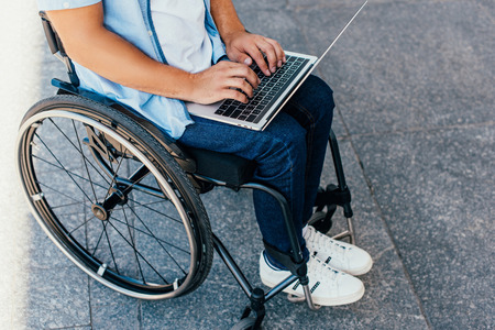 Cropped image of man in wheelchair using laptop on streetの写真素材