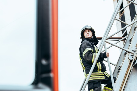 Female firefighter in protective uniform and helmet standing on ladder on streetの写真素材